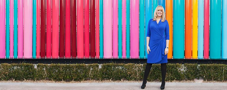 A woman in blue dress standing next to colorful wall.