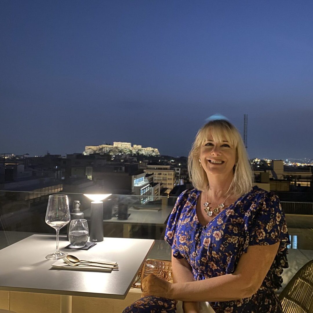 A woman sitting at an outdoor table with wine glasses.